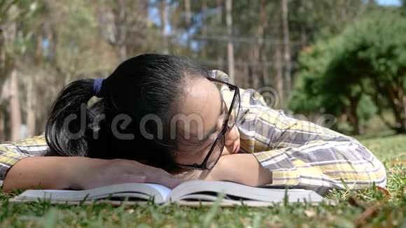 亚洲年轻女子放松和阅读一本书躺在公园的夏天活动和生活方式的概念视频的预览图