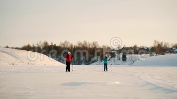 阳光明媚的一天一个女人和她的女儿在冰冻的湖面上滑雪女儿和母亲的冬季滑雪之旅视频的预览图