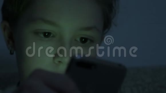 十几岁的女孩在黑暗的房间里使用智能手机视频的预览图