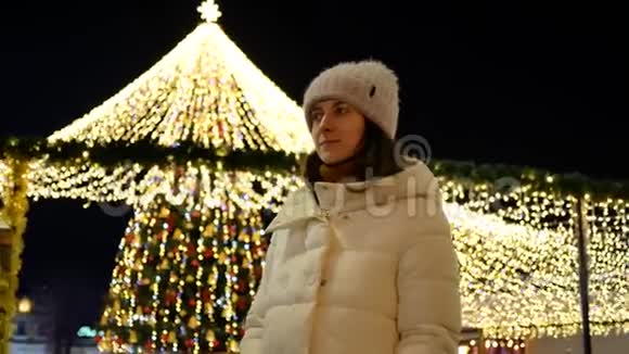 穿着外套戴着帽子的漂亮年轻女子在城市的圣诞树旁摆姿势视频的预览图