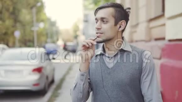 一个英俊的年轻人在城市里走来走去通过耳机在电话里交谈视频的预览图