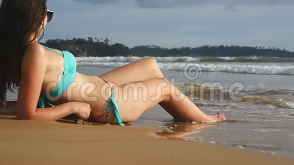 穿比基尼的漂亮女孩躺在海岸上在阳光明媚的日子放松年轻女子在海滨打日光浴深得人心视频的预览图