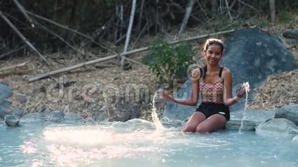 无忧无虑的年轻女人坐在温泉里的岩石上视频的预览图