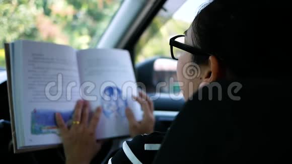 年轻女子在车里读一本书在城市街道上等待绿灯信号视频的预览图