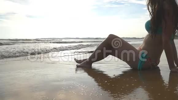 穿着泳衣的晒黑女人在海边放松欣赏美丽的风景穿比基尼的年轻女孩坐在海岸上视频的预览图