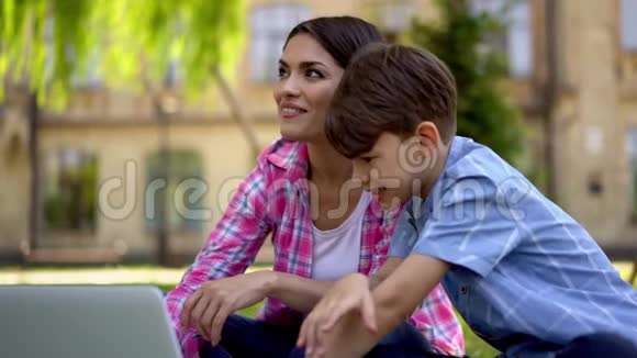 年轻的母亲在笔记本电脑上给儿子看家庭照片视频的预览图