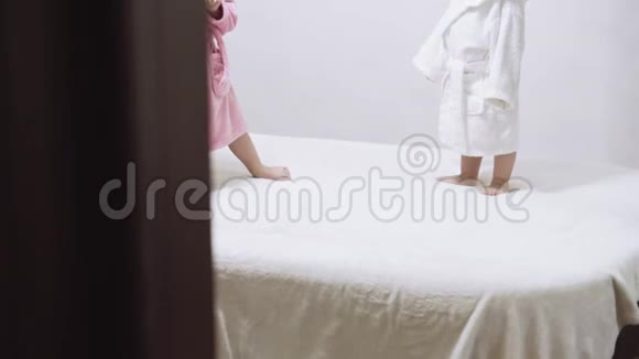 两个孩子穿着浴袍在一个白色背景和湿发后洗澡在白色床上洗澡后的男孩和女孩视频的预览图