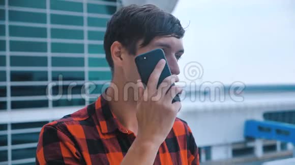 年轻人在机场大楼后台接电话在他的智能手机上聊天穿着红色格子衬衫视频的预览图
