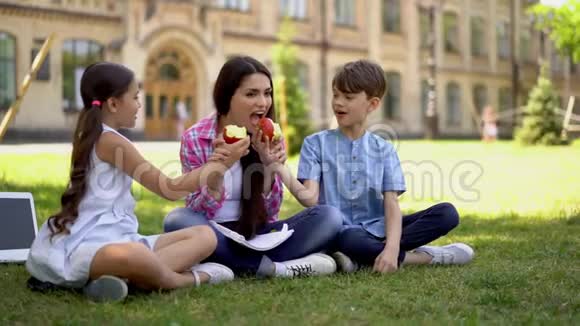 男孩和女孩和坐在户外的自由职业者母亲分享他们的苹果视频的预览图