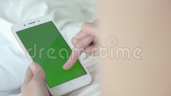 年轻女子躺着触摸和滑动绿色屏幕智能手机观看视频视频的预览图