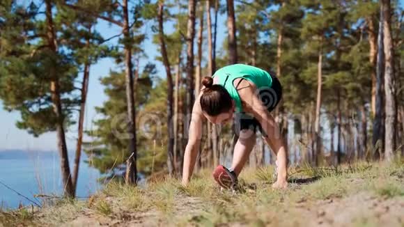 女孩跑步者在河岸上伸展腿部肌肉慢跑前热身视频的预览图