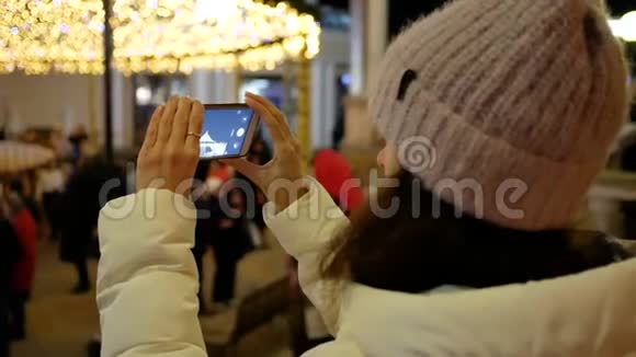 一位年轻女子在城市的圣诞树上打电话拍照从后面看视频的预览图