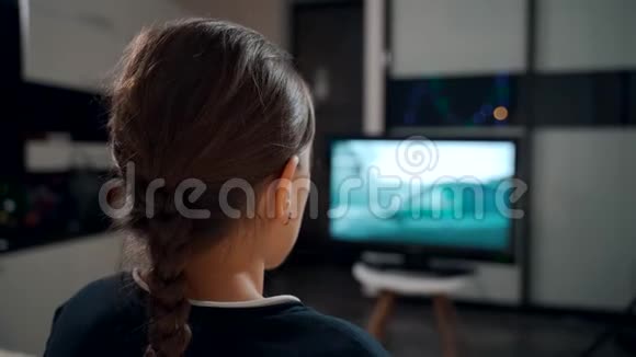 一个年轻女孩坐在沙发上看电视上的电影视频的预览图