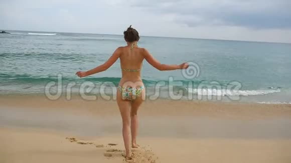 穿比基尼的快乐女人奔向海洋为了提神或游泳小女孩在沙滩上慢跑到海里视频的预览图
