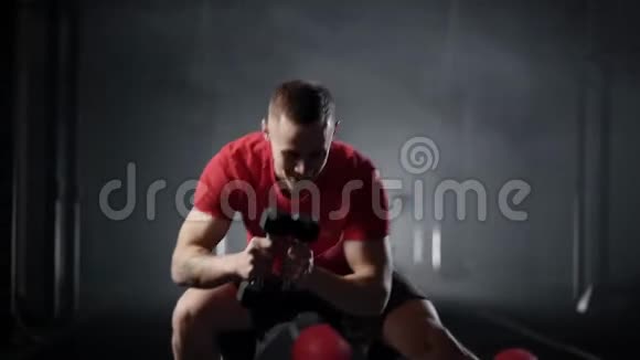 运动员们手里拿着哑铃蹲在黑暗的体操厅里训练腿和手保持身体健康视频的预览图