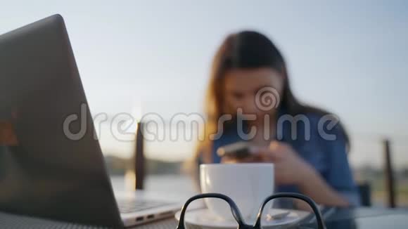 女孩正在智能手机上打字坐在街头咖啡馆的桌子旁专注于眼镜眼镜在桌子上还有视频的预览图