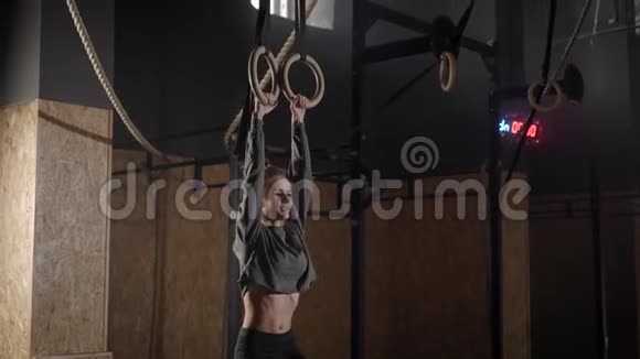 年轻女子在体操厅的吊环上吊着腿腹部肌肉紧张视频的预览图