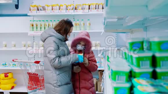 一个带着一个年轻女儿戴着医用口罩的女人在商店的乳制品部门视频的预览图