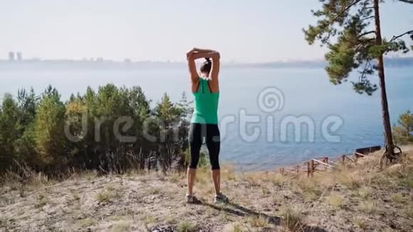 女孩跑步者在一条高河岸上伸展肌肉慢跑前热身视频的预览图