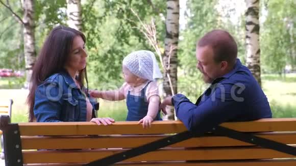 一家人爸爸妈妈和一个小女孩坐在城市公园的长椅上玩耍视频的预览图