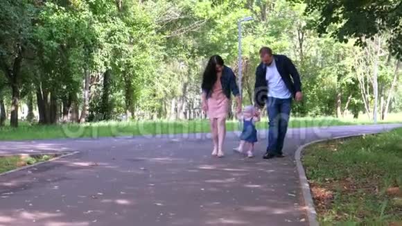 小女孩试图走第一步牵着爸爸妈妈手在城市公园视频的预览图
