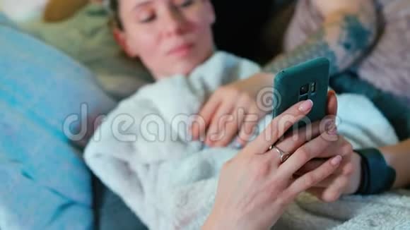 一个女人躺在沙发上在智能手机上写短信视频的预览图