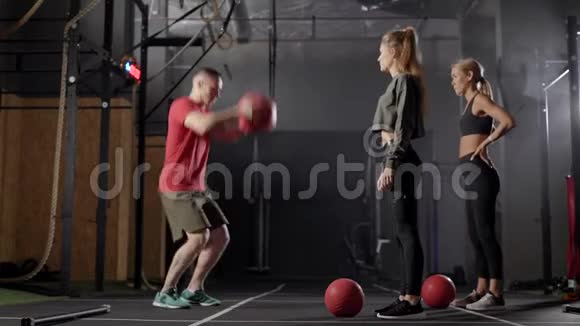 两名女运动员在体操馆与教练一起进行力量训练时用混合球重复练习视频的预览图