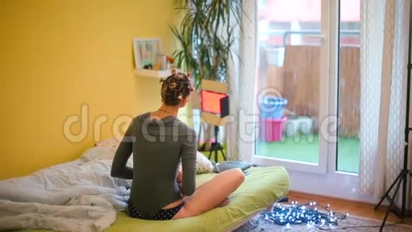 一个女人坐在房间里的床上一边看着窗外沉思视频的预览图