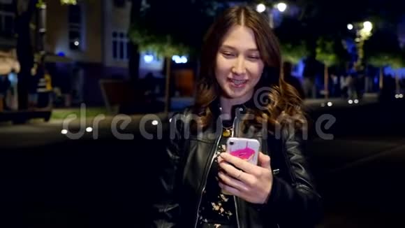 年轻女孩在晚上的街道上用照相机打电话视频的预览图