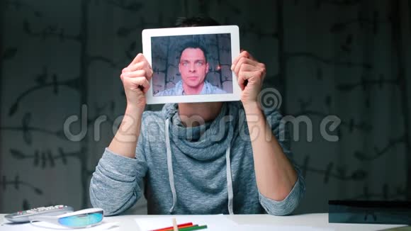 一个坐在桌子旁的人手里拿着平板电脑屏幕代替他的头视频的预览图