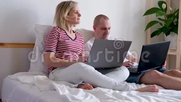 4k年轻的一家人在电脑旁的床上远程工作隔离夫妇冠状病毒呆在家里安全视频的预览图