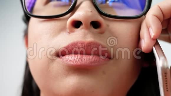 闭上不化妆的女性嘴唇肖像戴上眼镜在手机上愉快地说话微笑着专注于嘴唇视频的预览图