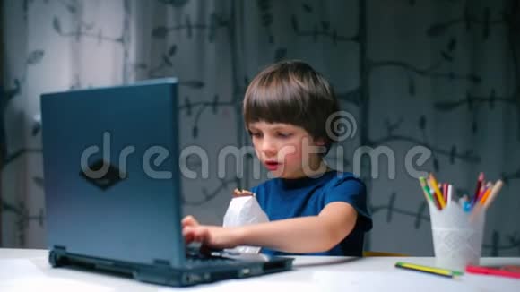 一个男孩坐在学校的办公桌前用笔记本电脑键盘打字视频的预览图
