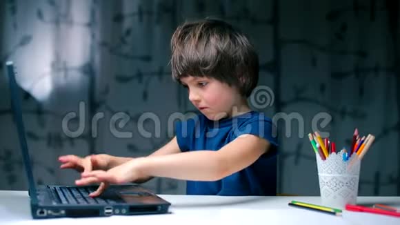 一个男孩坐在学校的桌子上按下笔记本电脑按钮视频的预览图