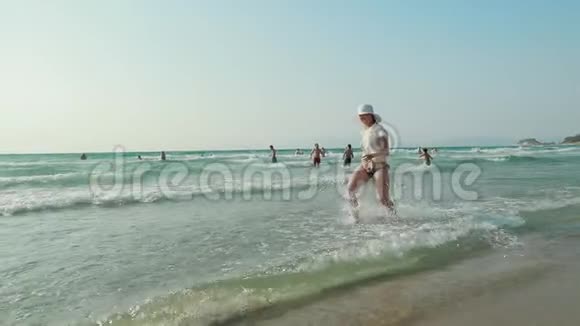 年轻的白种人女士穿着泳衣戴着夏帽在海水中飞溅在海洋海滩度假慢慢视频的预览图