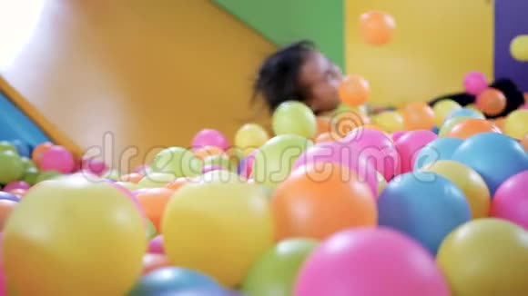 可爱的小女孩在塑料干池里玩滑梯里面有五颜六色的球在孩子们的操场室内视频的预览图