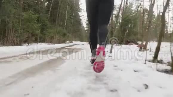 镜头跟随女孩的腿在雪道上慢跑森林里有水坑视频的预览图
