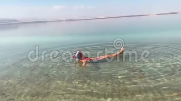 女人在死海里游泳有趣躺在背上在手机上拍照视频的预览图