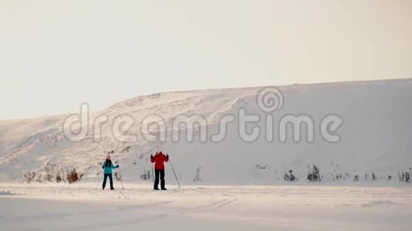 阳光明媚的一天一个女人和她的女儿在冰冻的湖面上滑雪女儿和母亲的冬季滑雪之旅视频的预览图