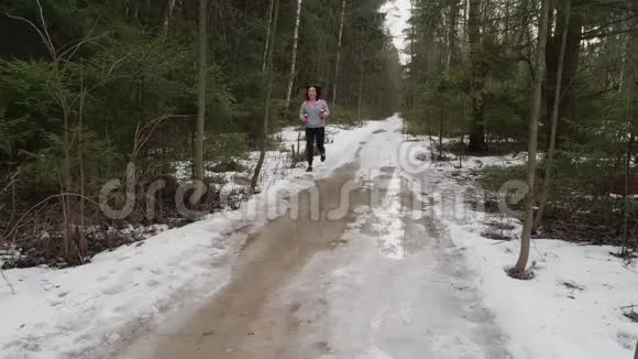 带着酒吧的女孩朝镜头跑过来绕着大水坑走在冬天的森林里慢跑视频的预览图