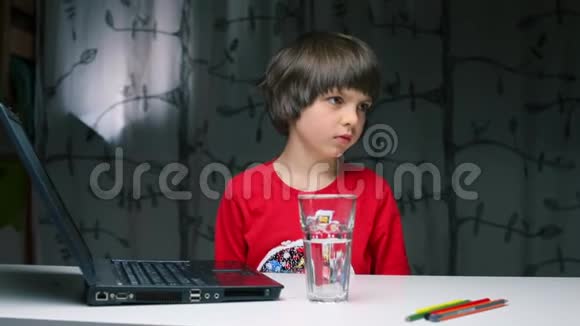 一个坐在桌子旁的男孩把杯子里的水倒到笔记本电脑上视频的预览图