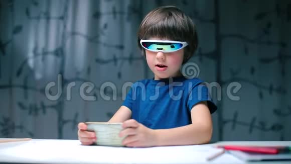 一个戴着现代眼镜的孩子坐在桌子旁使用智能手机视频的预览图