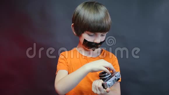 一个嘴上有黑色胶带的男孩检查一台旧相机视频的预览图
