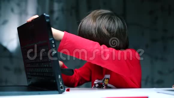 一个男孩坐在桌子旁检查笔记本电脑的背面视频的预览图