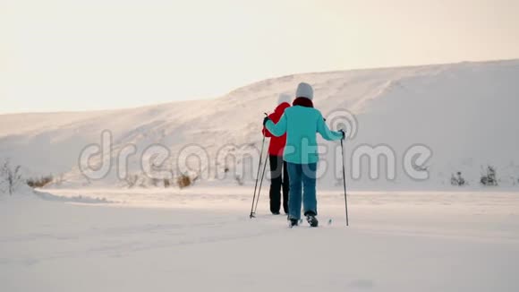 阳光明媚的一天一个女人和她的女儿在冰冻的湖面上滑雪女儿和母亲的冬季滑雪之旅视频的预览图