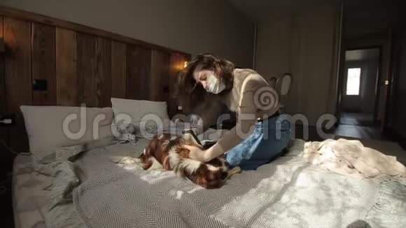 一个戴着防护面罩的年轻漂亮女孩正在家中检疫她的狗冠状病毒COVID19视频的预览图