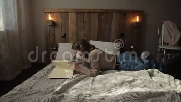一个年轻的欧洲女孩躺在她的房间里戴着防护面具在检疫期间翻了一本书冠状病毒COVID视频的预览图