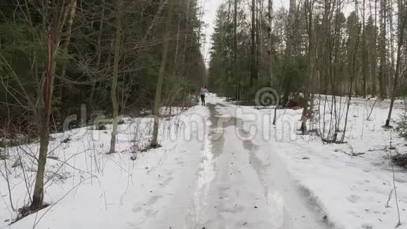 穿着运动服的女人朝镜头跑去她在森林里雪上奔跑冬天慢跑视频的预览图