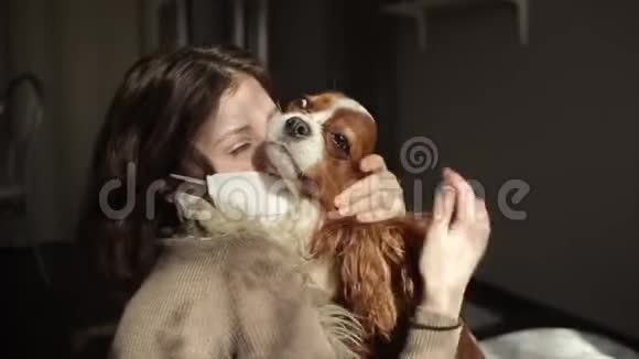 一个戴着防护面罩的漂亮女孩在家中隔离时拥抱和抚摸她的狗冠状病毒视频的预览图