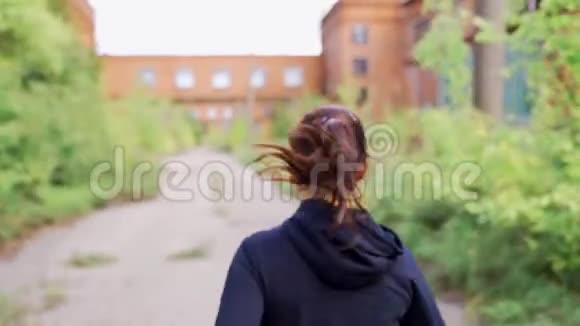 穿着黑色运动服的女孩穿过一家废弃工厂的领地视频的预览图